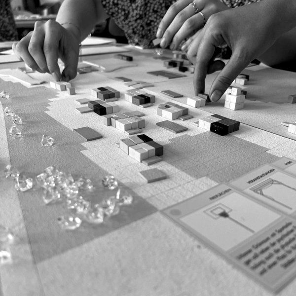 Hände setzen Bausteine auf ein Spielfeld, Planspiel Multiplex City